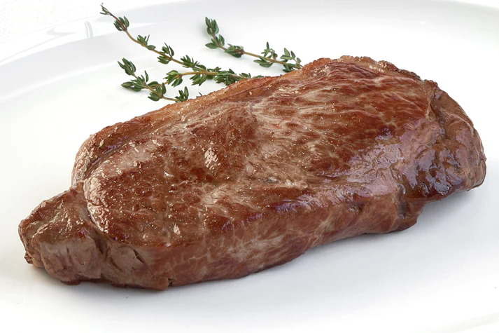 Cooked Grass-Fed Boneless New York Strip Steak from New York Prime Beef served on a white plate with herb garnish, tender and flavorful.