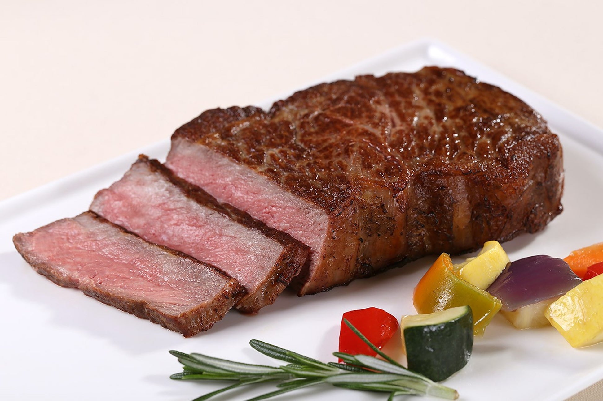 Dry aged USDA Prime Boneless New York Strip steak from New York Prime Beef, perfectly cooked and sliced, plated with roasted vegetables and rosemary for a premium steakhouse presentation