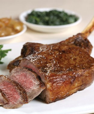 Dry aged USDA Prime Cowboy Ribeye steak from New York Prime Beef, bone-in and cooked to perfection, sliced to show tenderness and served with sides