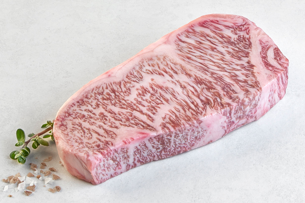 Raw Japanese A5 Wagyu Boneless New York Strip steak from New York Prime Beef, featuring intense marbling and tenderness, displayed horizontally on a white background with herbs