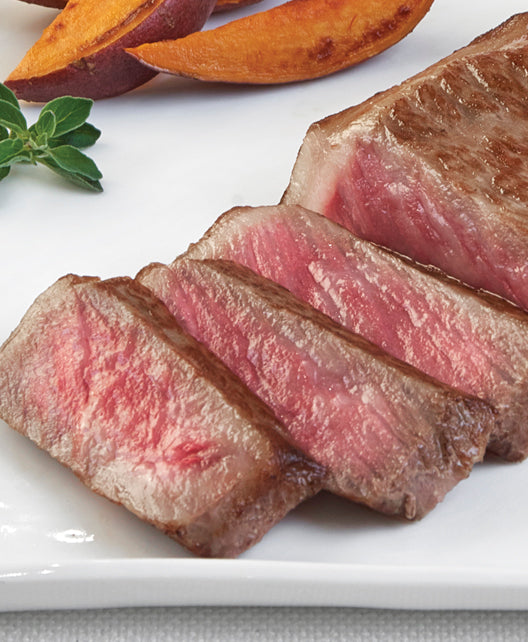 Japanese A5 Wagyu Boneless New York Strip steak from New York Prime Beef, cooked medium rare and sliced to highlight marbling and tenderness, plated horizontally with roasted sweet potato wedges for a gourmet steakhouse presentation