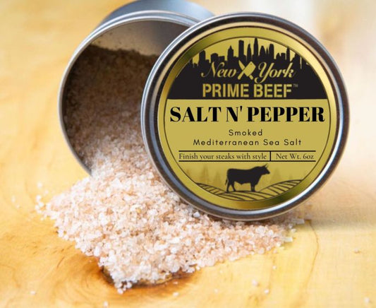 A shaker of smoked Mediterranean sea salt labeled 'Salt N' Pepper' by New York Prime Beef, with spilled salt visible in front of the container.