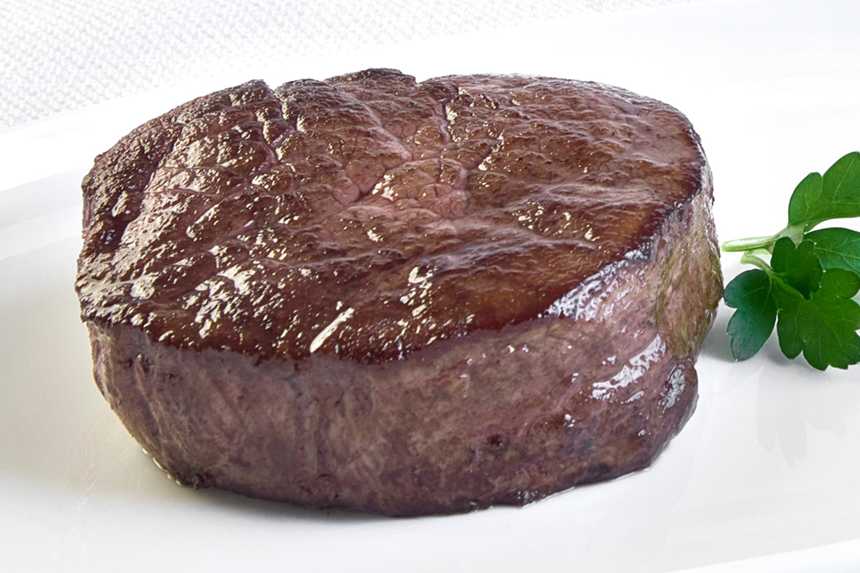 A single, cooked domestic wagyu Filet Mignon steak on a white plate with a sprig of parsley to the side.