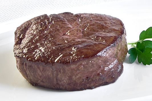 A single, cooked domestic wagyu Filet Mignon steak on a white plate with a sprig of parsley to the side.