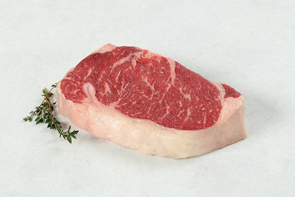 Raw Dry Aged USDA Prime Boneless New York Strip Steak from New York Prime Beef with visible marbling on a light background.