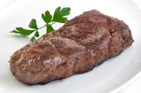 Cooked USDA Prime NY Strip Steak from New York Prime Beef, grilled to perfection and served on a white plate with fresh parsley garnish