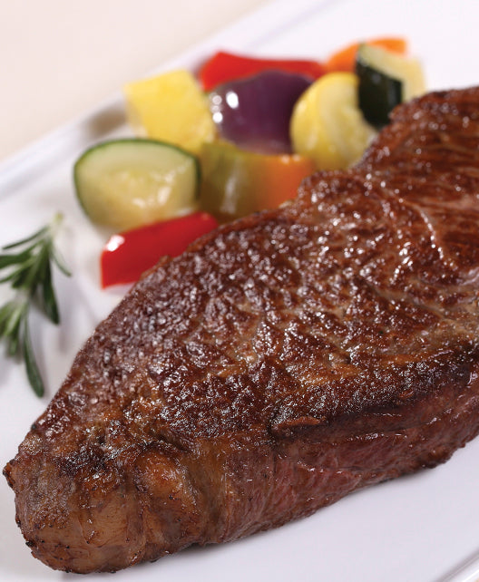 Cooked Dry-Aged USDA Prime Boneless New York Strip Steak from New York Prime Beef, seared to perfection with rich marbling, plated alongside fresh roasted vegetables for a gourmet steakhouse presentation