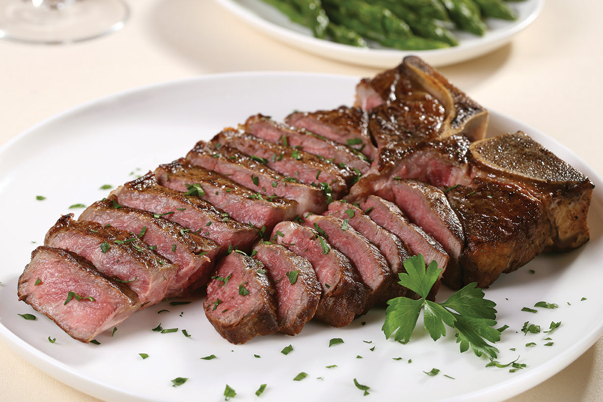 Dry aged USDA Prime T-Bone steak from New York Prime Beef, perfectly cooked and sliced to show tenderness and marbling, plated for a steakhouse presentation