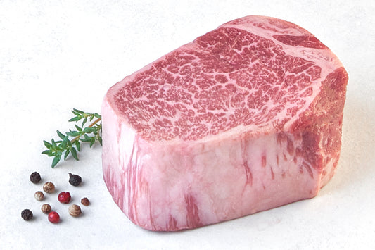 Raw Japanese A5 Wagyu Boneless Filet Mignon steak from New York Prime Beef, featuring exceptional marbling and thickness, displayed on a white background with herbs and peppercorns