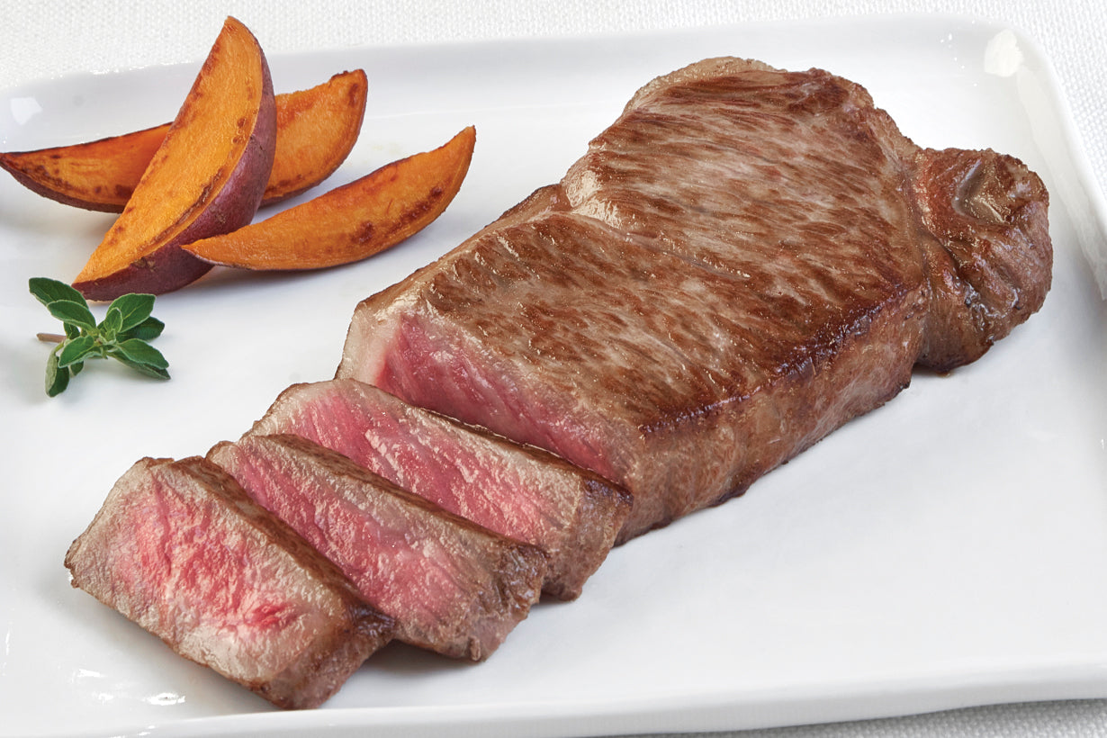 Japanese Wagyu Boneless New York Strip steak from New York Prime Beef, perfectly cooked and sliced to show marbling, served with sweet potato wedges