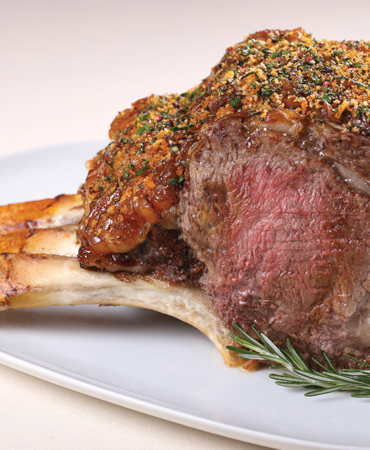 Cooked Dry-Aged USDA Prime 3-Bone Rib Roast from New York Prime Beef with herb crust, bone exposed, and rosemary garnish on a white plate.