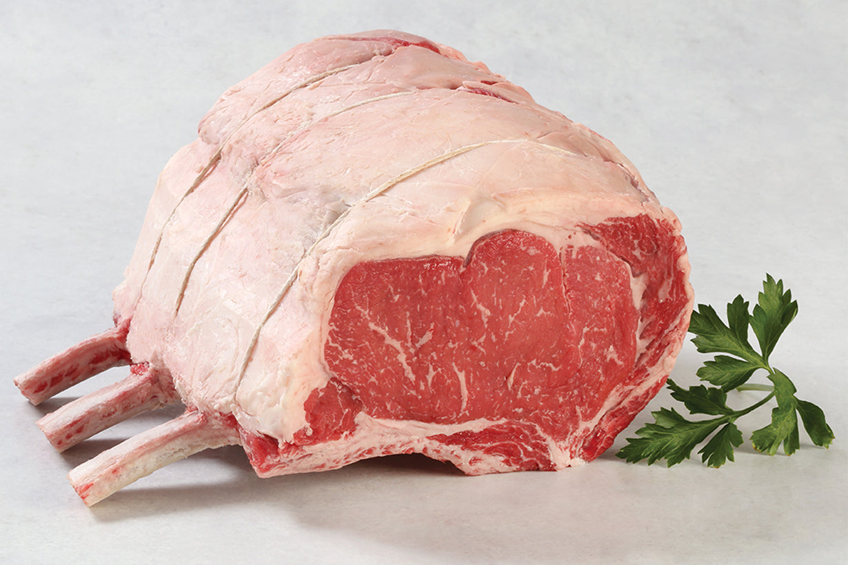 Cooked Dry-Aged USDA Prime 3-Bone Rib Roast from New York Prime Beef with herb crust, bone exposed, and rosemary garnish on a white plate.