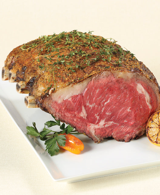 Cooked Dry-Aged USDA Prime 4-Bone Rib Roast from New York Prime Beef served on a white platter with herbs, parsley, and roasted vegetables.