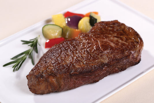 A cooked boneless Dry Aged USDA Prime New York strip steak from New York Prime Beef on a white plate with a side of vegetables and a sprig of rosemary.