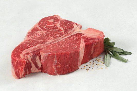 Raw Porterhouse Steak from New York Prime Beef with visible marbling, fresh thyme, and seasoning salt on a light background.